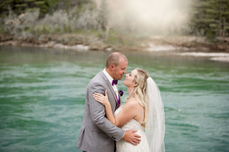 wedding couple almost kissing in front of turquoise water in alberta