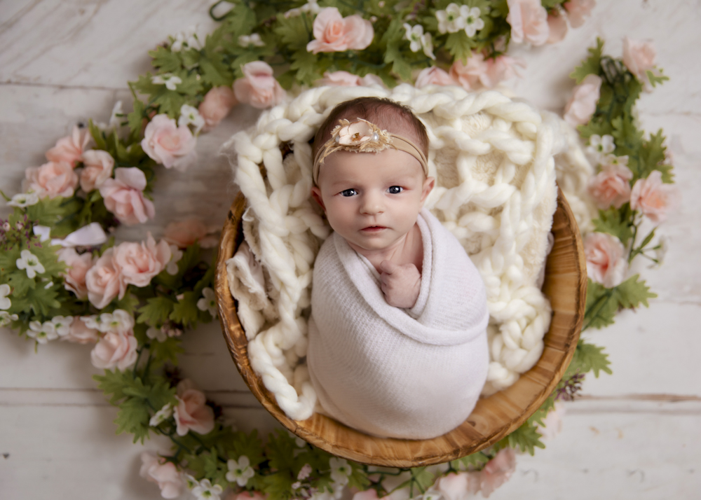 Newborn baby girl adorned with flowers in a wicker basket