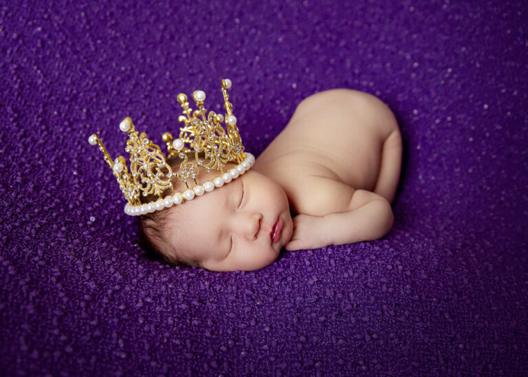 Sleeping queen newborn baby girl professional photos wearing a crown