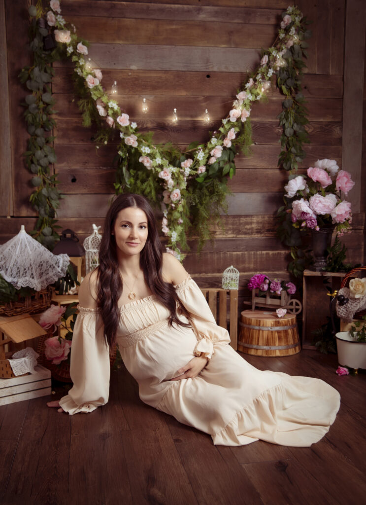 Gorgeous brunette sitting and lovingly cradling belly with flowers surrounding her