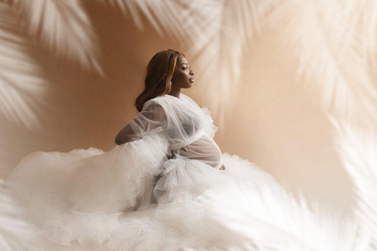 Elegant maternity photo of black woman in a white dress and leaves