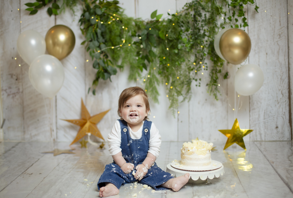 Child ready for a cake smash sitting beside a custom cake